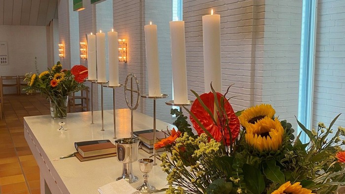Bord med blomster, lysstake og brød i lys og farverig kirke