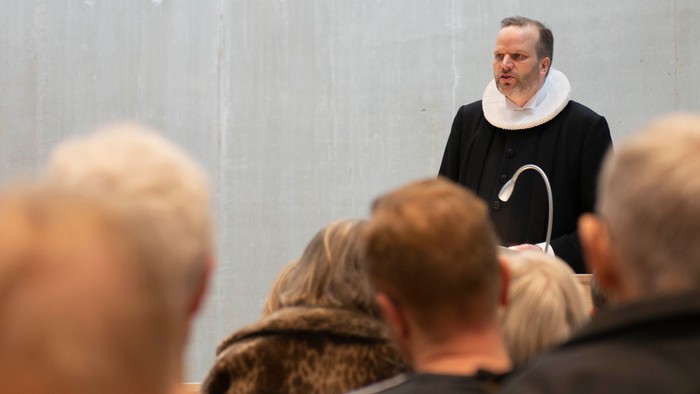 En mand i sort kappe holder foredrag for en gruppe mennesker.