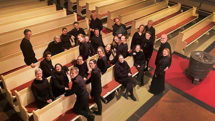 Chor in schwarzer Konzertkleidung locker in Kirchenbänken verteilt.