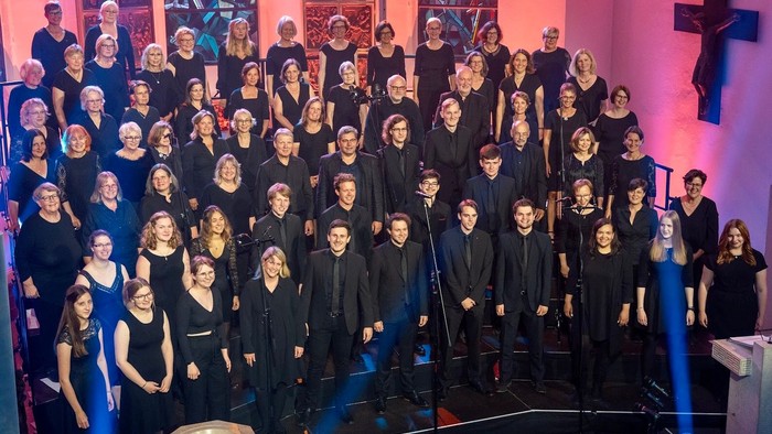 Große Gruppe von Menschen in dunklen Anzügen singt in einer Kirche