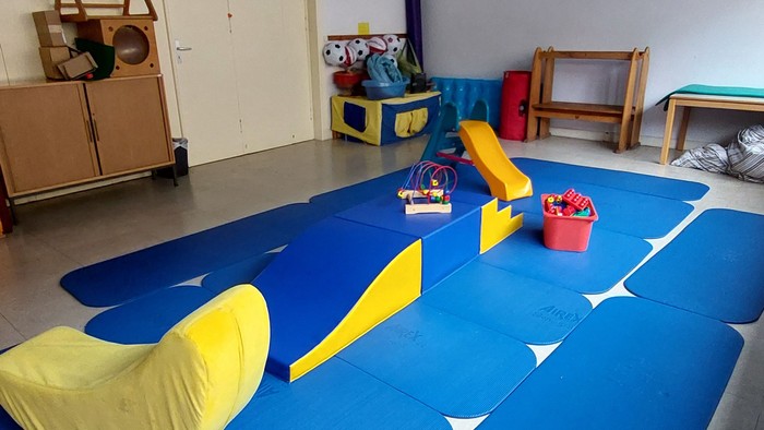 Ein Kinderzimmer mit blauen Matten, gelben Kissen und Spielzeug.