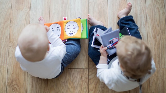 Zwei Kinder spielen auf dem Boden mit Büchern und einem Tablet.