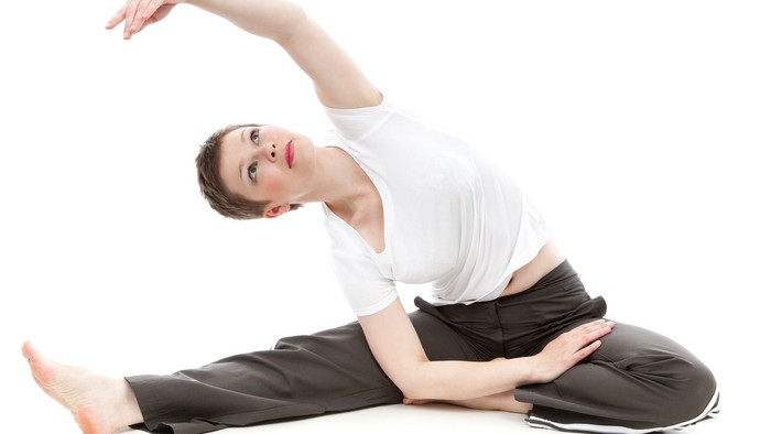 Frau in weißem Hemd und grauer Hose übt Yoga im Schneidersitz