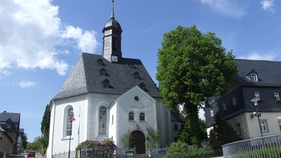 Weiße Kirche mit hohem Turm und Uhr, umgeben von Bäumen und Häusern