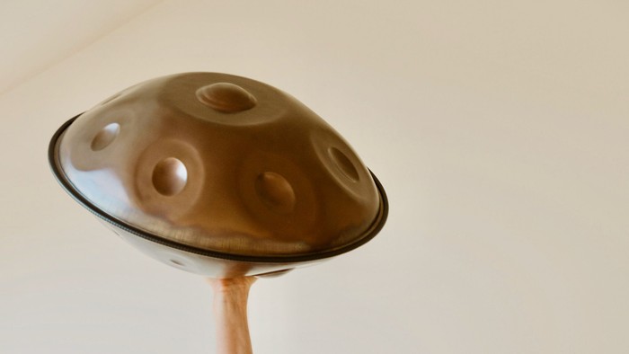 Eine metallene Klangschale mit mehreren eingedellten Stimmöffnungen auf einem Holzständer.