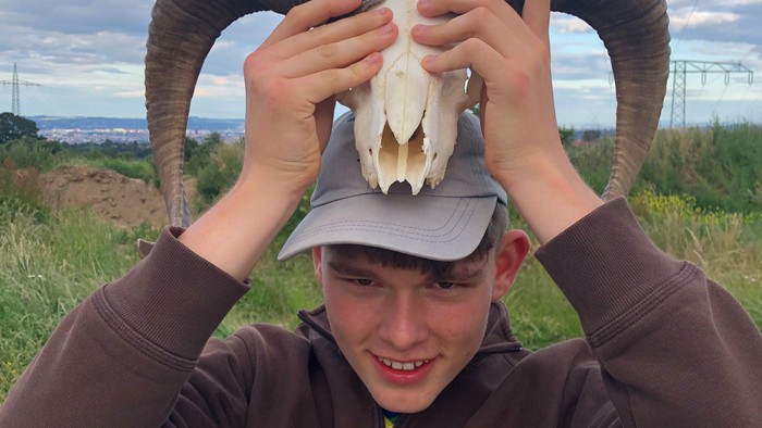 Junger Mann trägt Schafsschädel mit Hörnern auf dem Kopf