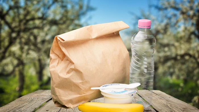 En papirpose, en plastflaske og en banan på bord i naturen