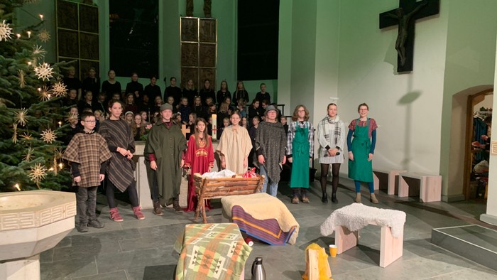 Eine Gruppe von Menschen in Kostümen posiert in einer Kirche vor einem Weihnachtsbaum und einer Krippe.