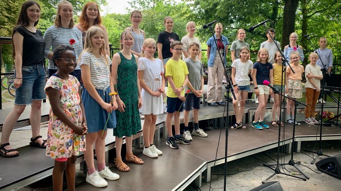 Eine Gruppe von Kindern und Jugendlichen steht auf einer Bühne und singt in Mikrofone.