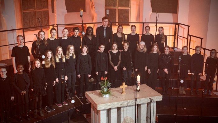 Ein Jugendchor und ein Dirigent posieren formell in einer Kirche mit einem kerzenbeleuchteten Altar.