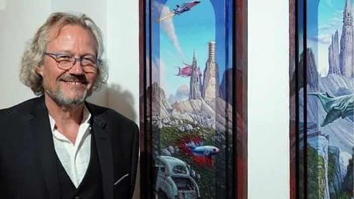 Un homme en costume pose à côté de peintures fantastiques.