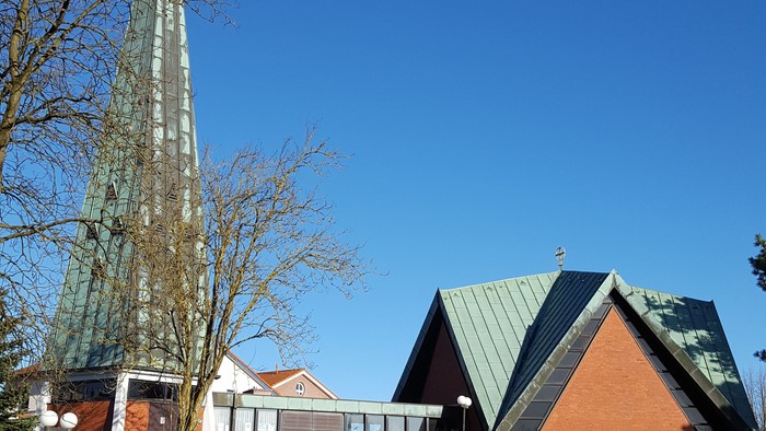 Kirche mit hohem Turm und spitzem Dach auf grünem Hügel unter blauem Himmel