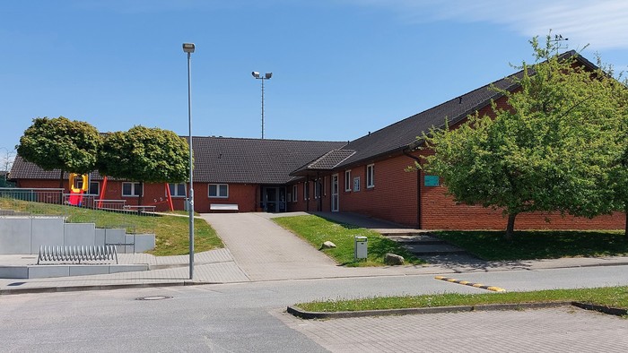 Ein rotes Backsteingebäude mit Parkplatz und Bäumen.