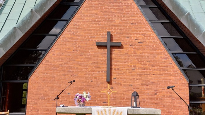 Vor einer Kirche steht ein Altar mit Kreuz und Blumen.