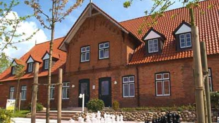 Ein großes, rotes Haus mit schwarzer Tür und Fenstern, umgeben von einem gepflegten Garten mit Kieswegen und Bäumen.