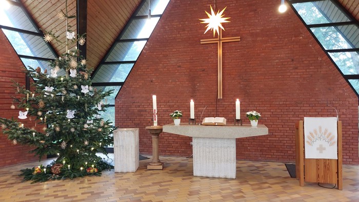 In der Kirche steht ein geschmückter Weihnachtsbaum neben einem Altar mit Kreuz und Kerzen.