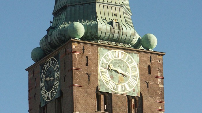 Der Uhrturm hat ein grünes Dach und Zifferblätter auf beiden Seiten.