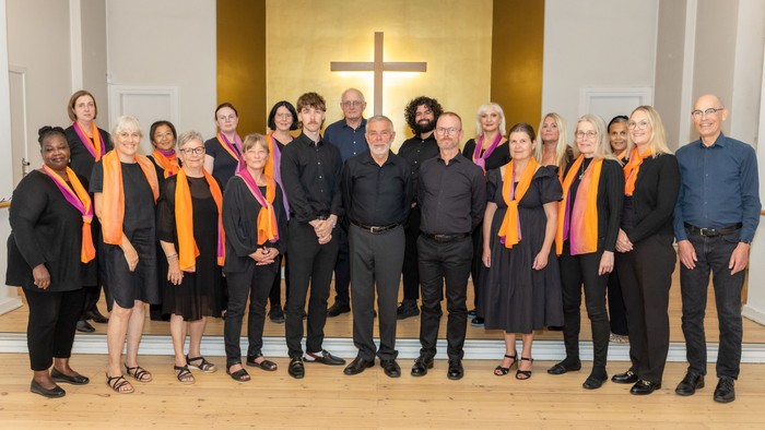 En gruppe af mennesker står sammen i en kirke, alle med orange bælter.