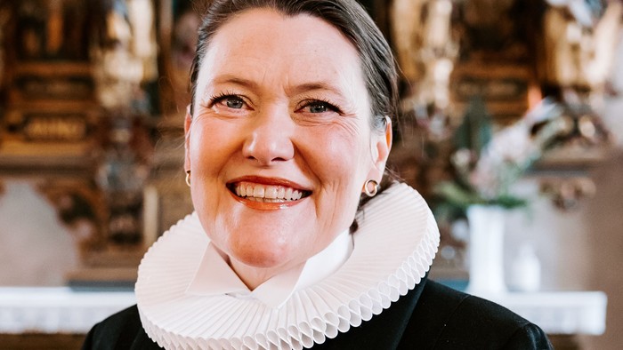 En kvinde i sort jakke med hvid krage står foran en prægtig altertavle.