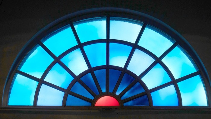 Ein buntes, halbrundes Fenster mit blauen und roten Farbtönen.