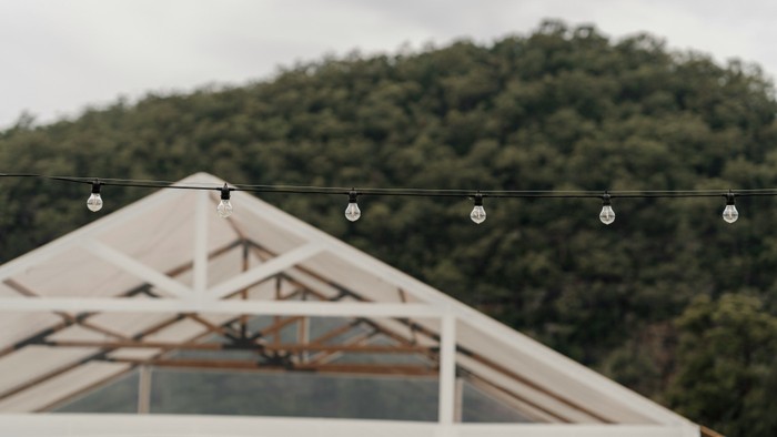 Elegante Outdoor-Zelt, geschmückt mit Lichterketten vor einem bewaldeten Hintergrund.