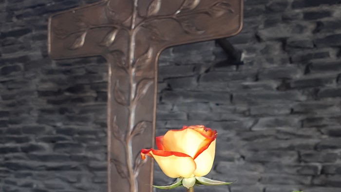 Ein Holzkreuz vor einem Blumenstrauß mit Sonnenblumen und Rosen