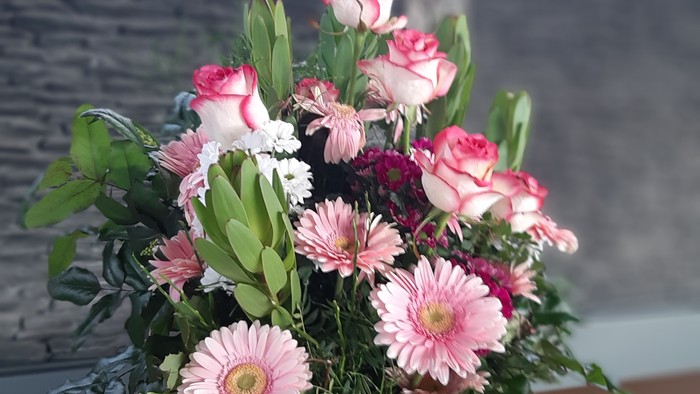 Blumenstrauß in Vase vor Kreuz an der Wand