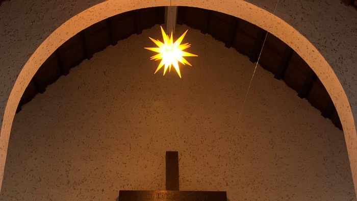 Ein Kreuz vor einer gewölbten Wand mit einer hellen Lichtquelle darüber