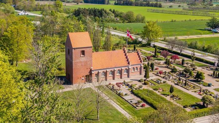 En stor rød murstenskirke i grønne landskab med vej og skov i nærheden
