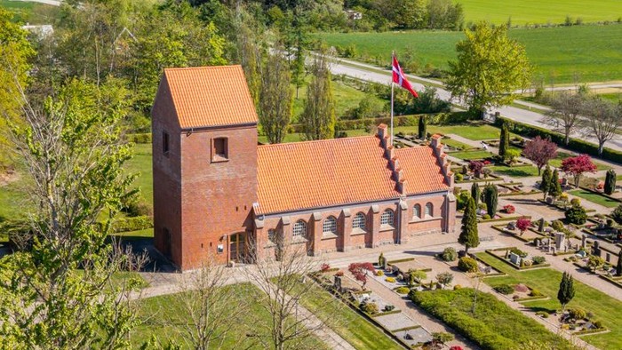 En stor rød murstenskirke i grønne landskab med vej og skov i nærheden