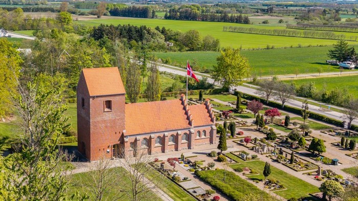 En stor rød murstenskirke i grønne landskab med vej og skov i nærheden
