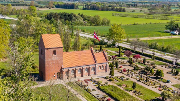 En stor rød murstenskirke i grønne landskab med vej og skov i nærheden
