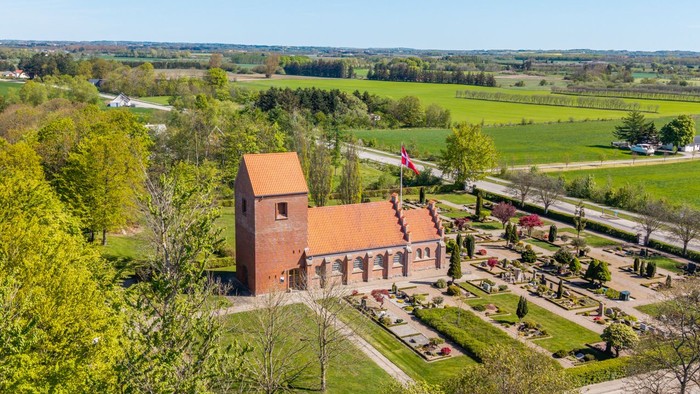 En stor rød murstenskirke i grønne landskab med vej og skov i nærheden