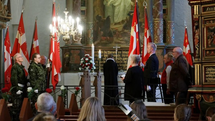 En kirke med several flag, en gruppe mennesker og en præst ved alteret