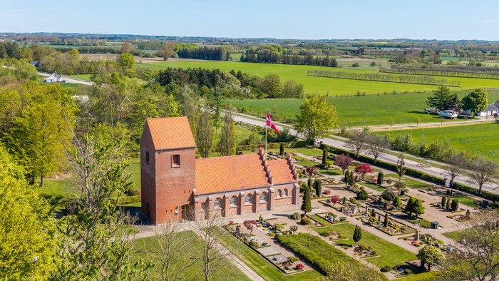 En stor rød murstenskirke i grønne landskab med vej og skov i nærheden