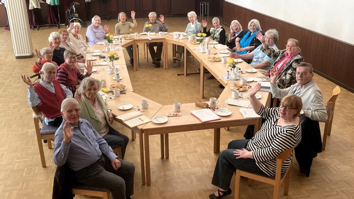 Eine Gruppe älterer Menschen sitzt an Tischen und isst gemeinsam.
