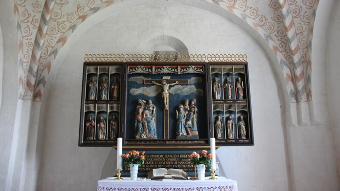 Alter Nr. Løgum kirke, hvorover der ses loftets buer med et kalkmaleri-mønster malet på i sarte farver.