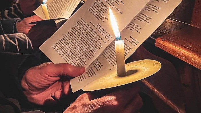 Hands holding lit candles and papers in dark setting