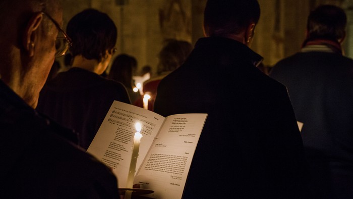 People holding lit candles and reading from books in a dimly lit room.