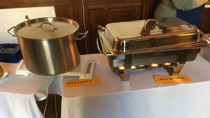 Auf dem Tisch stehen zwei große Metallbehälter mit Deckeln und kleinen Schildern 