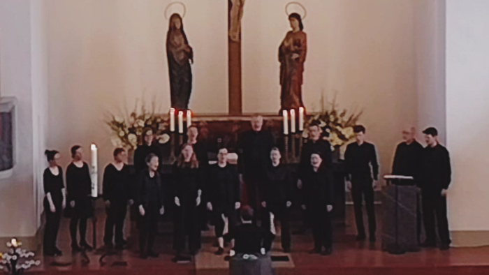 Ein Kirchenchor singt vor einem Kruzifix mit Marienstatue.