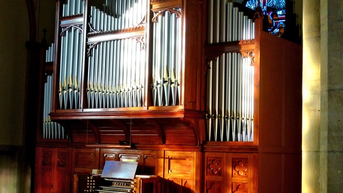 Große Kirchenorgel mit verzierten Holzpaneelen und farbigem Buntglasfenster