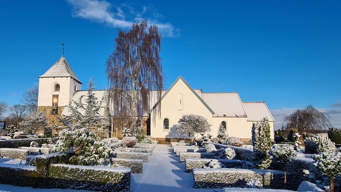 En snede kirke og gravlund under et klart blå himmel.