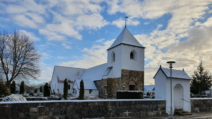 En lille kirke med tårn og tætte tag i sneklædt landskab