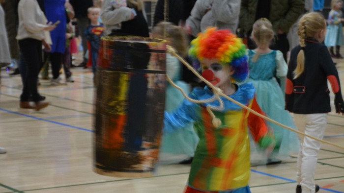 Barn i farverigt tøj danser med stang i sportshal.