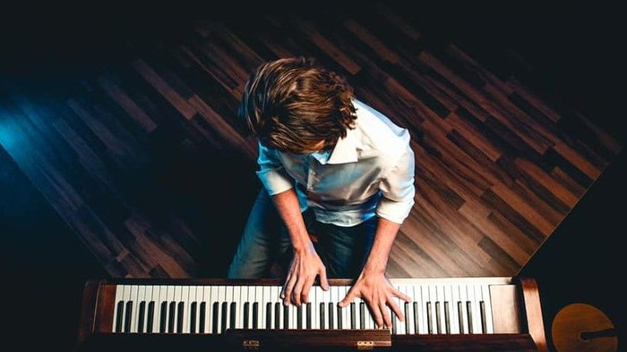 En ung pige spiller piano i en mørk rum.