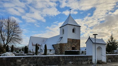 En lille kirke med tårn og tætte tag i sneklædt landskab