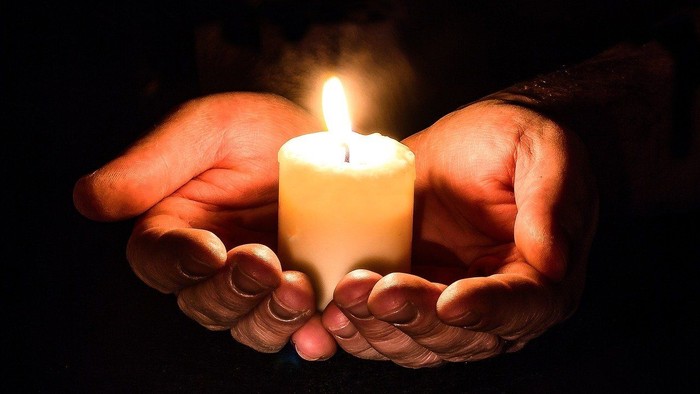 Hands gently holding a lit candle, creating a warm glow.