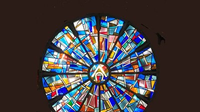 Buntes, kreisförmiges Mosaikfenster mit zentralem Symbol.