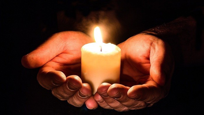 Hands gently holding a lit candle, creating a warm glow.